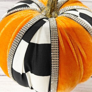 Pu&ograve; includere: Zucca di velluto arancione con tessuto a quadri bianco e nero e bordatura di strass.