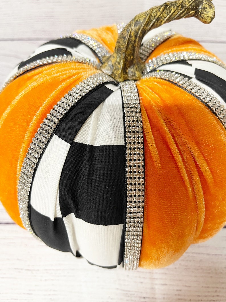 Pu&ograve; includere: Zucca di velluto arancione con tessuto a quadri bianco e nero e bordatura di strass.