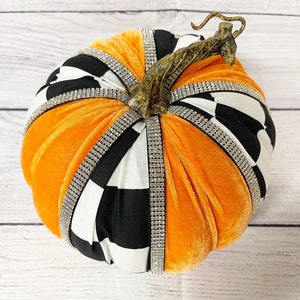 Pu&ograve; includere: Una zucca di stoffa a scacchi bianchi e neri con dettagli in velluto arancione e uno stelo dorato. La zucca &egrave; decorata con strass.