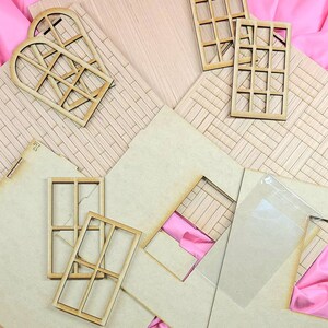 May include: A collection of unfinished light-colored wooden laser-cut pieces for a dollhouse assembly, including flat wall panels with etched brick patterns, two arched window frames, four rectangular window frames, and a clear plastic sheet.