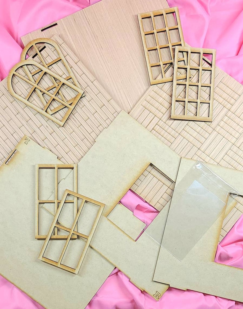 May include: A collection of unfinished light-colored wooden laser-cut pieces for a dollhouse assembly, including flat wall panels with etched brick patterns, two arched window frames, four rectangular window frames, and a clear plastic sheet.