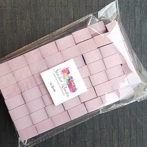 May include: A bag of 50 pink wooden craft blocks, perfect for miniature crafts and model building. The bag is labeled "Scaled Realm Miniature Crafts & Collections by Piecette."