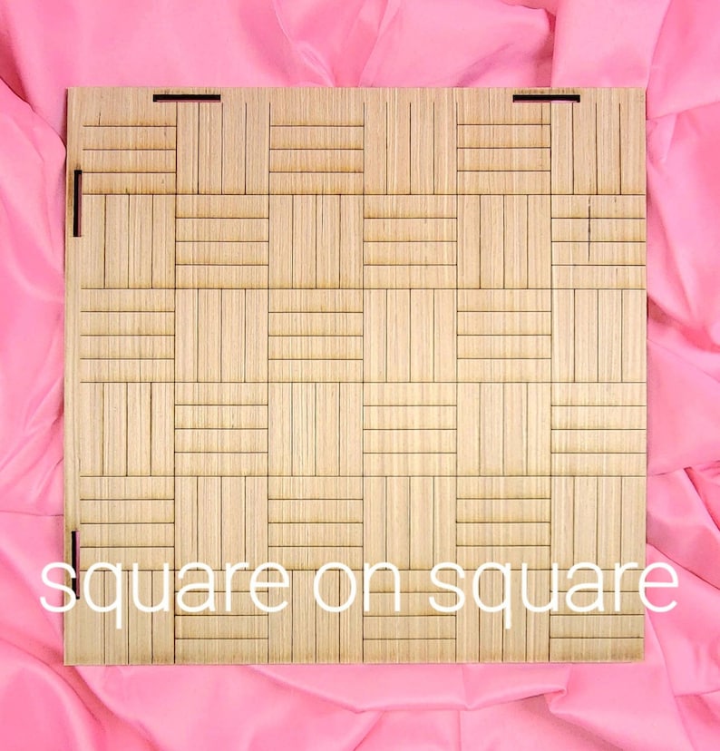 May include: A square wooden panel featuring a grid pattern of alternating vertical and horizontal slats. The light brown wood surface displays a geometric texture. The text "square on square" is printed in white at the bottom of the panel.
