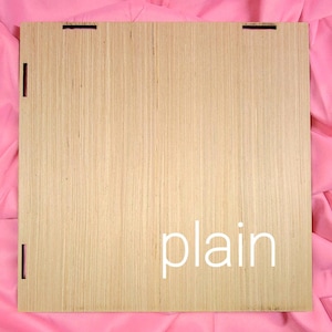 May include: A square light brown wooden panel with a natural wood grain texture. The panel features small rectangular cutouts along the edges for assembly. The word plain is printed in white lowercase letters on the lower right side of the panel.