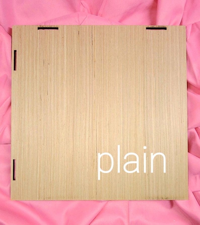 May include: A square light brown wooden panel with a natural wood grain texture. The panel features small rectangular cutouts along the edges for assembly. The word plain is printed in white lowercase letters on the lower right side of the panel.