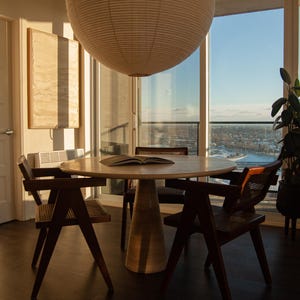 May include: A modern dining room set with a round wooden table and four chairs. A large paper lantern hangs above the table. The room has large windows with a view of the city.