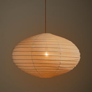 May include: A round, off-white paper pendant lamp with a ribbed texture and horizontal wire structure. The light fixture is suspended by a thin, dark brown cord, emitting a soft, warm glow from the center, creating a diffused lighting effect.