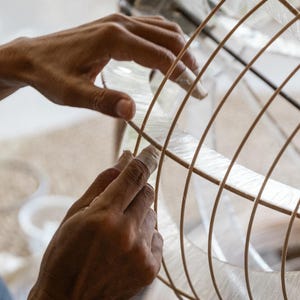 Peut inclure: Une structure sph&eacute;rique compos&eacute;e de fines nervures en bois clair dispos&eacute;es en grille, avec un mat&eacute;riau fibreux translucide et p&acirc;le superpos&eacute; entre les lattes de bois incurv&eacute;es pour former un objet arrondi en forme de cage.