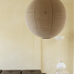 May include: A large, spherical, beige paper pendant light hangs from the ceiling. The shade features a ribbed texture with horizontal lines. The light is suspended by a thin cord, creating a soft, diffused illumination within the interior space.