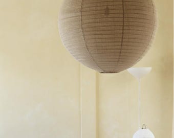 May include: A large, spherical, beige paper pendant light hangs from the ceiling. The shade features a ribbed texture with horizontal lines. The light is suspended by a thin cord, creating a soft, diffused illumination within the interior space.