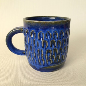 May include: A blue ceramic mug with a textured design. The mug has a brown rim and a dark blue glaze.