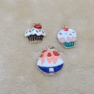 May include: Three gold-tone charms featuring a cupcake with white frosting and red sprinkles, a cupcake with pink frosting and red sprinkles, and a blue and white ice cream cone with a red strawberry on top.