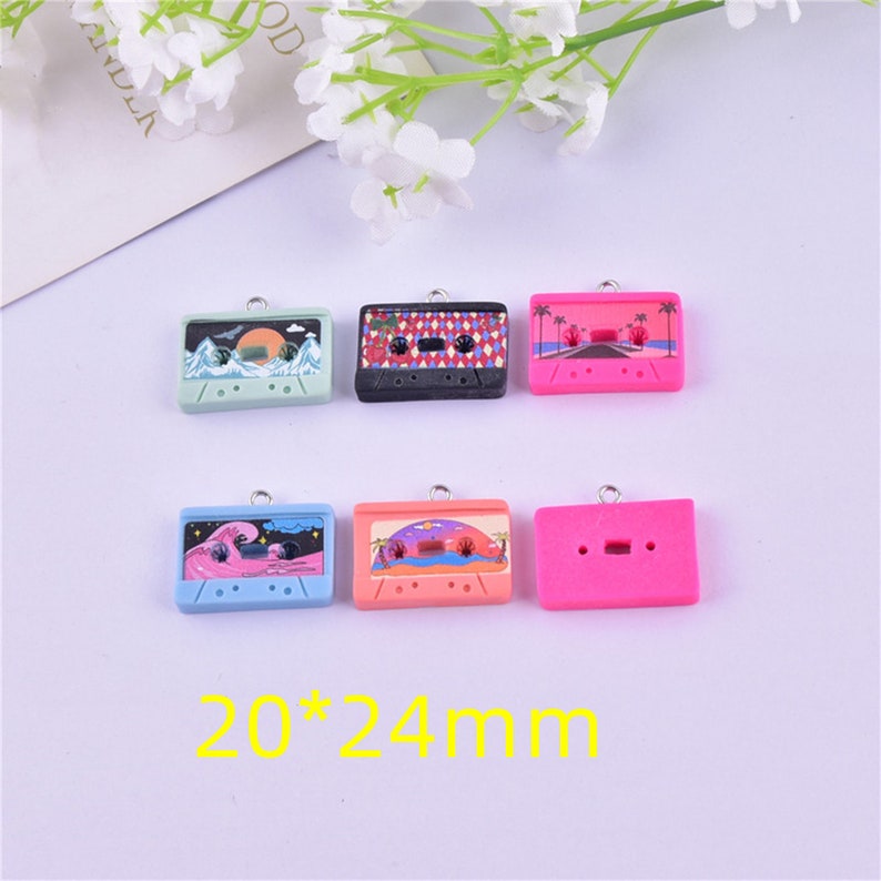 May include: Six colorful cassette tape charms with different designs, including a sunset, palm trees, and waves. The charms are 20mm by 24mm and have a silver loop for attaching to jewelry or other crafts.