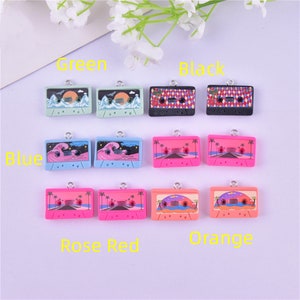 May include: Twelve colorful cassette tape charms with different designs, including palm trees, waves, and mountains. The charms are arranged in three rows of four, with each row labeled with a color: Green, Blue, Rose Red, and Orange. The charms are made of polymer clay and have a silver loop for attaching to jewelry or other crafts.
