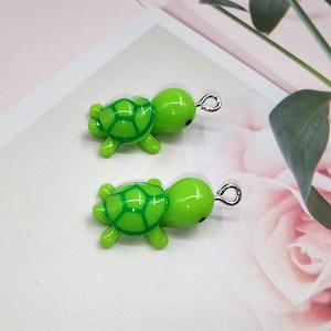 May include: Two green turtle charms with silver jump rings. The turtles have a green shell with a darker green pattern and black eyes.
