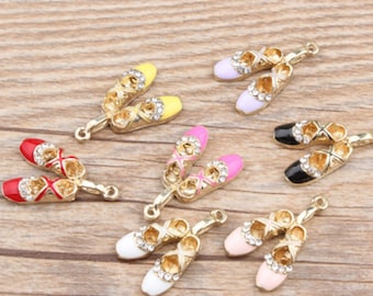 Pode incluir: Uma coleção de pingentes de sapatilhas de ballet douradas em várias cores, incluindo vermelho, amarelo, rosa, branco, preto e lavanda. Cada pingente apresenta detalhes de strass e uma argola para fixar em joias ou outros trabalhos manuais.