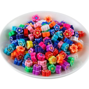 May include: A bowl filled with colorful flower-shaped polymer clay beads. The beads are in various colors, including red, orange, yellow, green, blue, purple, and pink.