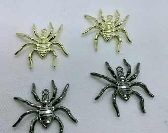 May include: Four metal spider charms in gold and gunmetal gray. Each spider has eight legs and a small loop at the top for attaching to jewelry or other crafts. The spiders are detailed with segmented bodies.