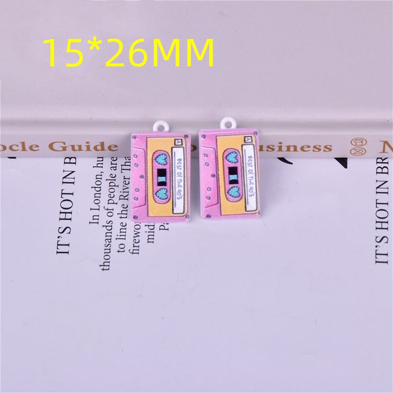 May include: Two pink and yellow cassette tape charms with blue hearts. The charms are approximately 1.5 by 2.6 centimeters.
