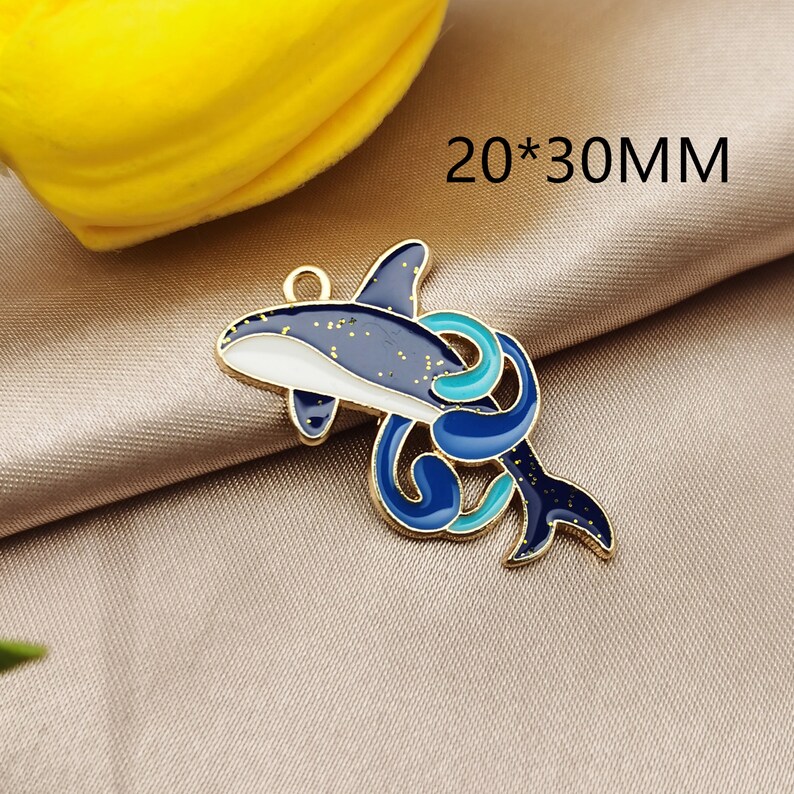 May include: Gold-tone metal charm featuring a blue and white dolphin with a blue and turquoise swirl design. The charm measures 20 x 30 mm.