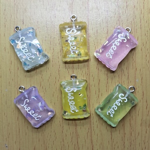 May include: Six colorful resin charms shaped like candy bags with the word "Sweet" written on them. Each charm has a different color and glitter embedded in the resin.