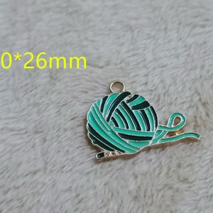 May include: A green and black enamel charm shaped like a ball of yarn with a gold metal loop. The charm measures 20mm by 26mm.