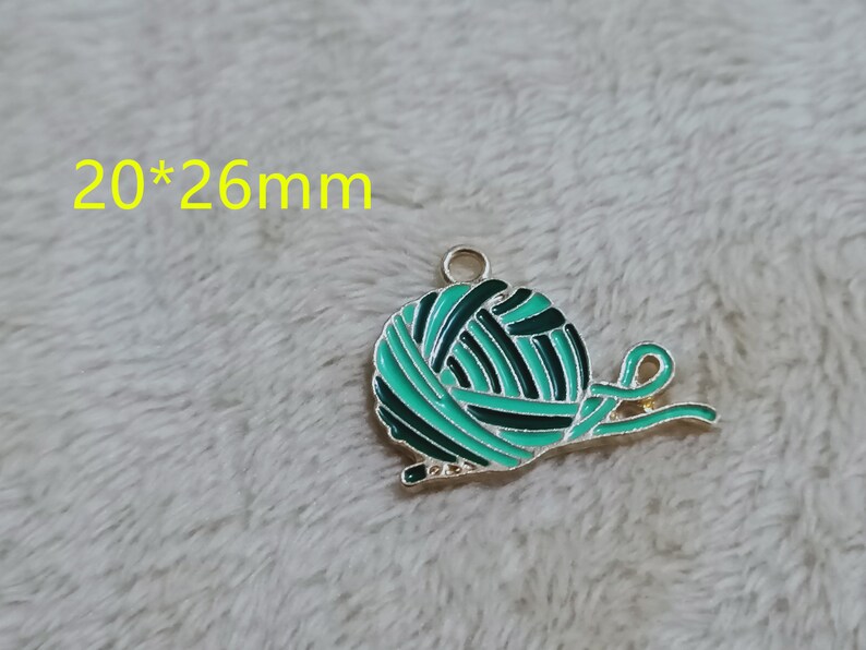 May include: A green and black enamel charm shaped like a ball of yarn with a gold metal loop. The charm measures 20mm by 26mm.