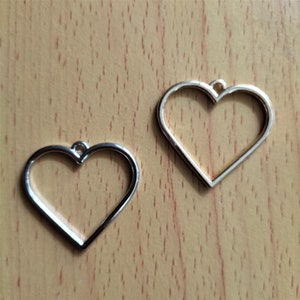 May include: Two silver metal heart-shaped frames with a loop at the top for hanging.
