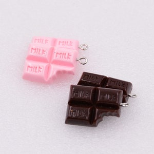 May include: Two chocolate bar charms, one pink and one brown, with the word "MILK" printed on each section. Both charms have a silver jump ring attached.