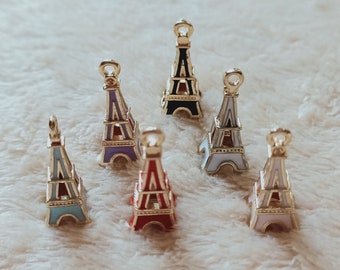 Pode incluir: Seis encantos da Torre Eiffel em miniatura em diferentes cores, incluindo preto, roxo, branco, azul, vermelho e rosa. Os encantos são feitos de metal e têm um acabamento dourado.