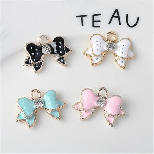 May include: Four gold-tone bow charms with white rhinestones. The bows are black with white polka dots, white with black polka dots, light blue with white polka dots, and pink with white polka dots.