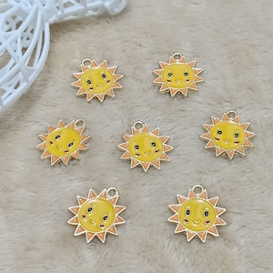 May include: Seven gold-colored charms shaped like suns with yellow and orange faces. The charms have a loop at the top for attaching to a necklace or bracelet.
