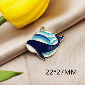 May include: Gold-tone metal charm featuring a blue and white whale with a wavy pattern. The charm measures 22 x 27 mm.