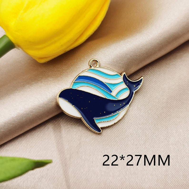 May include: Gold-tone metal charm featuring a blue and white whale with a wavy pattern. The charm measures 22 x 27 mm.