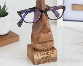 May include: Wooden glasses holder shaped like a face with a nose that holds glasses. The base of the holder is engraved with the text "Grandad Bob's Glasses".