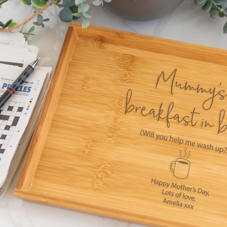 Pode incluir: Uma bandeja de caf&eacute; da manh&atilde; retangular de bambu com texto gravado. O texto diz "Mummy's breakfast in b" com texto adicional e um gr&aacute;fico de x&iacute;cara de caf&eacute;. Um jornal e uma caneta s&atilde;o vis&iacute;veis &agrave; esquerda.