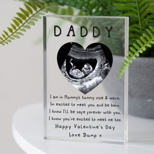 May include: A clear acrylic block with a black and white ultrasound image inside a heart shape. The text "DADDY" is at the top of the block. The text below the image reads: "I am in Mummy's tummy nice & warm. I'm excited to meet you and be born. I know I'll be safe forever with you. I know you're excited to meet me too. Happy Valentine's Day Love Bump x"