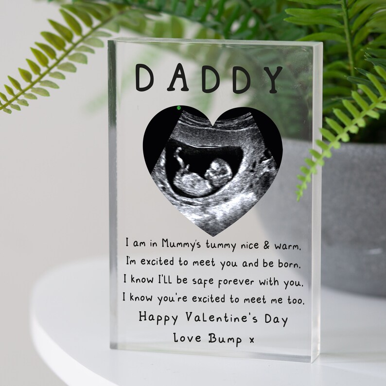 May include: A clear acrylic block with a black and white ultrasound image inside a heart shape. The text "DADDY" is at the top of the block. The text below the image reads: "I am in Mummy's tummy nice & warm. I'm excited to meet you and be born. I know I'll be safe forever with you. I know you're excited to meet me too. Happy Valentine's Day Love Bump x"