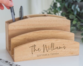 May include: A light-colored wooden desk organizer with multiple compartments for pens and letters. The organizer has a curved design and features the engraved text "The Williams LETTERS & THINGS". Two pens are in the pen holder.