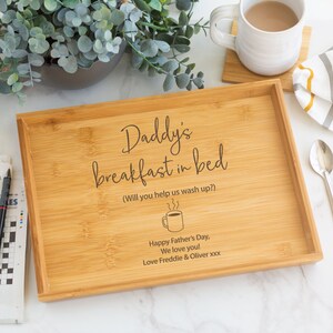 Pode incluir: Bandeja de caf&eacute; da manh&atilde; retangular de bambu com a inscri&ccedil;&atilde;o "Daddy's breakfast in bed" e "Happy Father's Day, We love you!". A bandeja tem uma borda elevada e um desenho de x&iacute;cara de caf&eacute;. Uma caneca de caf&eacute; e uma palavras cruzadas tamb&eacute;m s&atilde;o vis&iacute;veis.