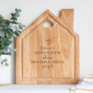 Op de afbeelding: Houten snijplank in de vorm van een huis met de tekst "Welcome to Nanny's House where Braydon & Amelia get spoilt" erop gegraveerd.