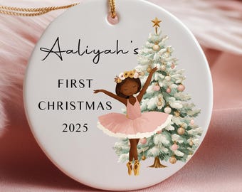 May include: A round white ceramic Christmas ornament with a gold string. The ornament has the text "Aaliyah's FIRST CHRISTMAS 2025". A ballerina in a pink tutu and a Christmas tree are illustrated.