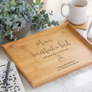 Pode incluir: Uma bandeja de caf&eacute; da manh&atilde; retangular de bambu com texto gravado. O texto diz "Mum's breakfast in bed" e "Happy 60th Birthday!". Uma caneca de ch&aacute;, uma planta e uma palavras cruzadas tamb&eacute;m s&atilde;o vis&iacute;veis.