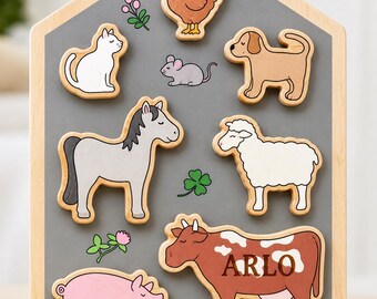 Peut inclure: Un plateau de puzzle en bois en forme de maison avec un centre gris comportant des découpes pour un poulet, un chat, une souris, un chien, un cheval, un mouton, un cochon et une vache. La vache porte le nom ARLO et la base est gravée LOVE NANNY & GRANDAD XXX.