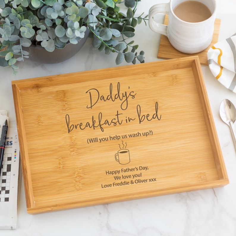 Pode incluir: Uma bandeja retangular de bambu com o texto "Daddy's breakfast in bed" e um desenho de ch&aacute;vena de caf&eacute;. A bandeja inclui o texto "Happy Father's Day, We love you! Love Freddie & Oliver xxx". Uma caneca de caf&eacute; e uma palavra cruzada est&atilde;o no fundo.