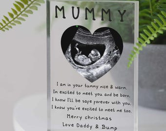 May include: A clear acrylic block with the word "MUMMY" at the top. A heart-shaped cutout reveals a grayscale ultrasound image of a fetus. Text below reads "I am in your tummy...Merry Christmas, Love Daddy & Bump."