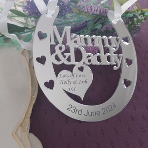 Pu&ograve; includere: Ciondolo a forma di ferro di cavallo argentato con le parole "Mommy & Daddy" e un cuore con il testo "Lots of Love Holly & Josh xxx" e la data "23rd June 2024".