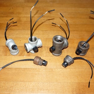 May include: Five different types of electrical outlet adapters with black wires attached. The adapters are made of metal and have a silver finish.