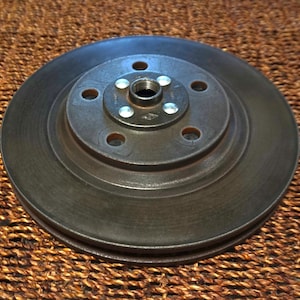 May include: A black metal disc with a smaller metal disc in the center. The center disc has five holes and a central hole with a threaded insert.