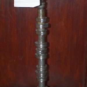 May include: A toilet paper holder made from a repurposed car part. The holder is made of metal and has a white toilet paper roll on top. The holder is mounted on a wooden surface.